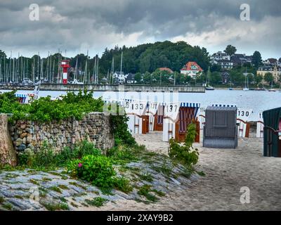 Strand mit nummerierten Liegen, Booten im Wasser und Leuchtturm im Hintergrund, Eckernförde, Schleswig-Holstein, Deutschland Stockfoto