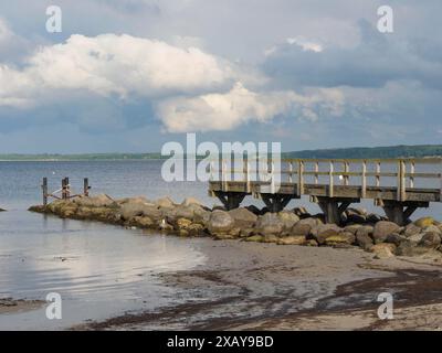 Holzsteg führt ins Meer, Steinhaufen an der Küste, Wolken am Himmel, Eckernförde, Schleswig-Holstein, Deutschland Stockfoto