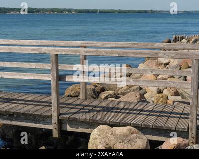 Eine hölzerne Fußgängerbrücke über ein felsiges Ufer eines ruhigen Sees unter blauem Himmel im Sommer, Flensburg, Schleswig-Holstein, Deutschland Stockfoto