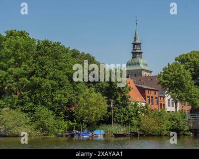 Ein Kirchturm und Gebäude am Uferufer mit Bäumen und Booten im Wasser, friedrichstadt, schleswig-holstein, deutschland Stockfoto