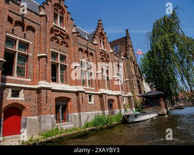 Eine Reihe historischer Backsteingebäude am Ufer mit roten Türen und Natur im Hintergrund, Brügge, Belgien Stockfoto