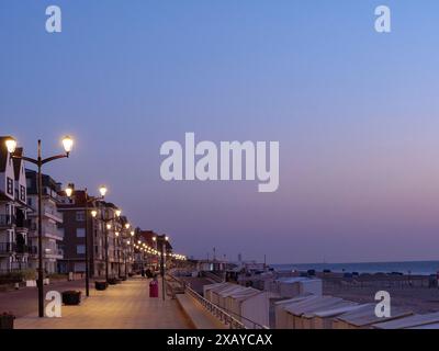 Eine beleuchtete Promenade mit Laternen und Gebäuden in der Abenddämmerung am Strand, de haan, Belgien Stockfoto