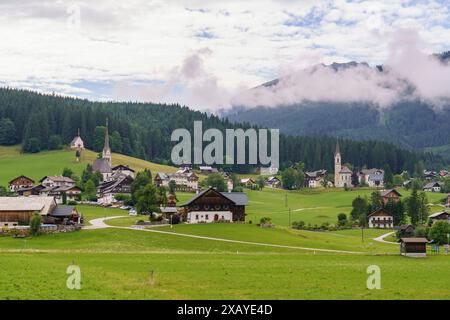 Ein malerischer Blick auf ein Dorf mit Kirchen und Häusern, eingebettet in eine grüne Landschaft und eingerahmt von Bergen und Wolken, Gosau, Österreich Stockfoto