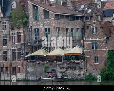 Alte Backsteingebäude mit Terrassen und Booten entlang eines Ufers in der Stadt Gent, Belgien Stockfoto