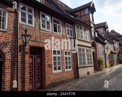 Das Foto zeigt eine gepflegte Straße mit historischen Backsteinhäusern und nostalgischen Lampen entlang der Kopfsteinpflasterstraße in lüneburg Stockfoto