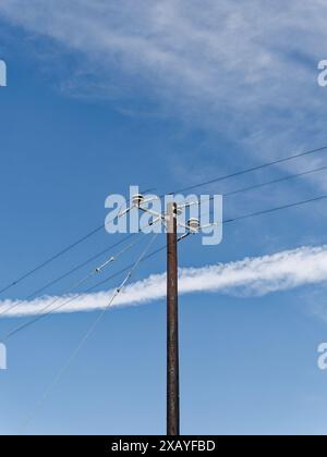 Ein verrosteter Versorgungsmast mit Isolatoren und Drähten steht vor einem bewölkten Himmel und zeigt veraltete elektrische Infrastruktur. Stockfoto