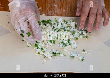 Eine Frau gibt eine Mischung aus Käse und Petersilie in einen traditionellen türkischen Pfannkuchen. Stockfoto