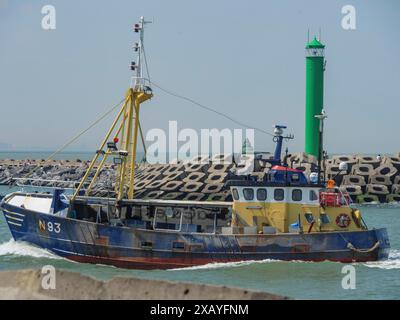 Ein Fischerboot mit der Nummer N93 fährt im Hafen neben einem grünen Leuchtturm bei ruhigem Wetter in oostende, Belgien Stockfoto