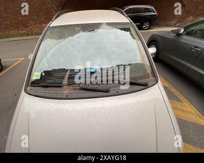 Schmutziges silbernes Auto parkt auf einer Stadtstraße, bedeckt mit dickem Staub und Schmutz, symbolisiert Verschmutzung und Vernachlässigung in städtischen Gebieten Stockfoto