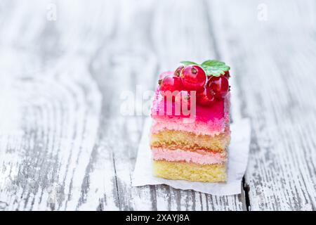 Stück des mehrschichtigen Beerenkuchens mit frischer roter Johannisbeere auf weißem Tisch Stockfoto