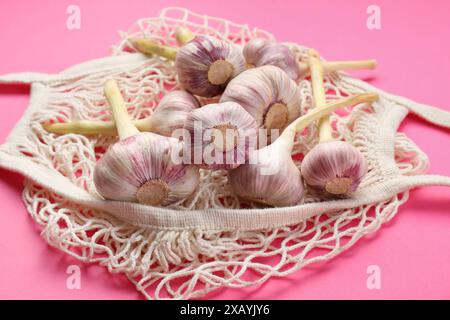 Schnur-Beutel mit Knoblauchköpfen auf hellrosa Hintergrund, Nahaufnahme Stockfoto