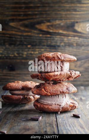 Schokoladen-Schokoladen-Eis-Cookie-Sandwiches, die mit Stückchen Schokoladenbonbons zubereitet und mit Milchschokolade-Eis über einem dunklen rustikalen Hintergrund gefüllt sind Stockfoto