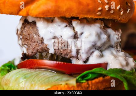 Saftiger Cheeseburger mit Rindfleisch, Salat, Tomaten, Gurken und cremiger Sauce, alles zwischen einem Sesambrötchen Stockfoto