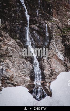 Eine atemberaubende Nahaufnahme eines Wasserfalls, der die zerklüfteten, eiskalten Hänge eines alaskischen Gletschers hinunterstürzt. Die kontrastierenden Texturen und die natürliche Schönheit machen dies aus Stockfoto