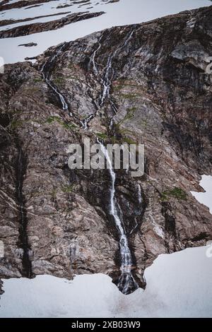 Diese atemberaubende Aufnahme fängt einen Wasserfall ein, der über schroffe Felswände auf einem Gletscher Alaskas stürzt und den dramatischen Kontrast zwischen Eis und r zeigt Stockfoto