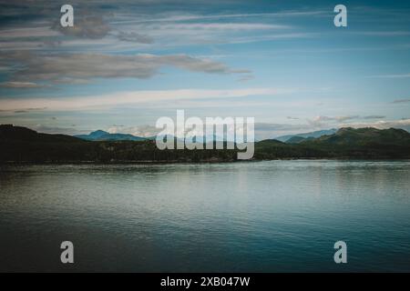 Dieses atemberaubende Foto fängt die ruhige Schönheit der Wildnis Alaskas mit üppigen grünen Hügeln und ruhigen Gewässern unter einem klaren blauen Himmel ein Stockfoto