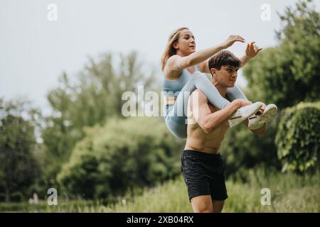 Junge Frau, die bauchmuskeln macht, während sie auf den Schultern ihres Freundes im Park sitzt Stockfoto