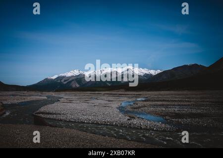 Entdecken Sie die raue Schönheit der Flussbetten Alaskas vor dem Hintergrund schneebedeckter Berge. Diese atemberaubende Landschaft fängt das Wesen der Wildnis ein Stockfoto