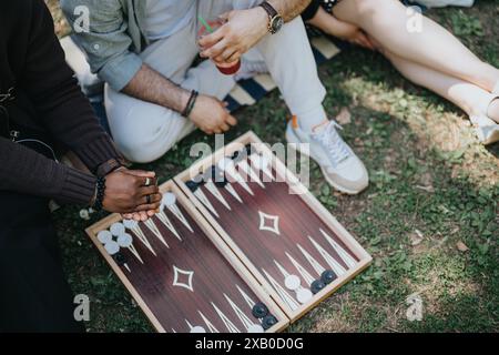 Multirassische Freunde, die an einem sonnigen Tag im Park eine Partie Backgammon genießen und sich glücklich und unbeschwert fühlen Stockfoto