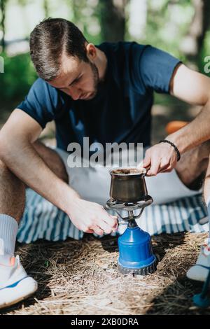 Mann, der im Freien Kaffee mit einem tragbaren Gasherd während eines Campingausflugs im Wald brütet Stockfoto