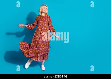 Foto in voller Länge der entzückenden schönen Frau tragen braunes Kleid, das Spaß hat, lächelnd aussehend leeren Raum isolierter blauer Hintergrund Stockfoto