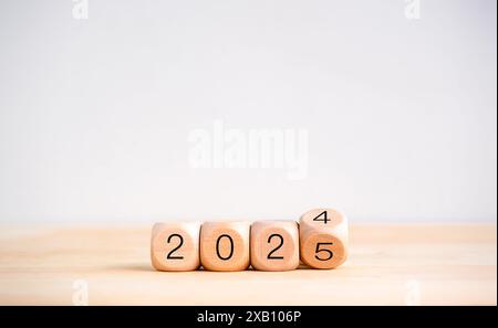 2025 ein frohes neues Jahr mit dem Wechsel zum Konzept der neuen Ära. Umkehren der 2024- bis 2025-Jahres-Kalendernummern auf Holzwürfelblöcken isoliert auf Holztisch und W Stockfoto