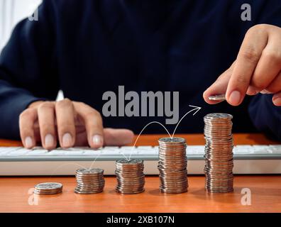 Der Pfeil springt auf der Grafik zum Wachstum von Geldmünzen auf dem Schreibtisch, während der Geschäftsmann eine Münze darauf legte. Online-Investitionen, Kosteneinsparungen, Online-Buchhaltung, Stockfoto