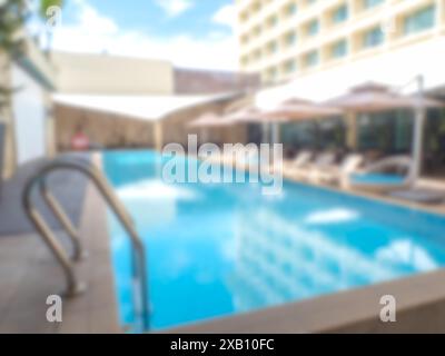 Abstrakter, unscharfer Außenpool mit Grifftreppe und Liegestühlen, Sonnenschirme im großen Gebäude des Hotels für Hintergrund und Tapeten. Verschwommenes V Stockfoto