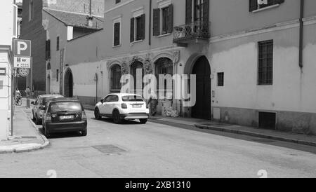 Cremona, Italien - 16. Mai 2024 Schwarzweißbild einer Frau, die mit geparkten Autos auf einer typisch italienischen Straße läuft Stockfoto