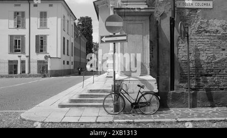 Schwarz-weiß-Bild eines Vintage-Fahrrads, das sich an einer Stange auf einer verlassenen italienischen Straße lehnt, mit einem Geschäftsmann, der im Hintergrund läuft Stockfoto