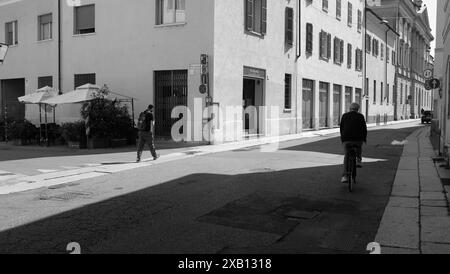 Cremona, Italien - 16. Mai 2024 Student mit Rucksack geht zu Fuß und ein Seniorenmann radelt auf einer schmalen Straße in einer europäischen Stadt Stockfoto