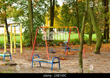 Ein Park mit hohen Bäumen im Herbst, gelben Blättern auf dem Rasen und einer Kinderschaukel. Stockfoto