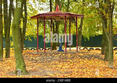 Park mit hohen Bäumen im Herbst, gelben Blättern auf dem Rasen und einem Pavillon. Stockfoto