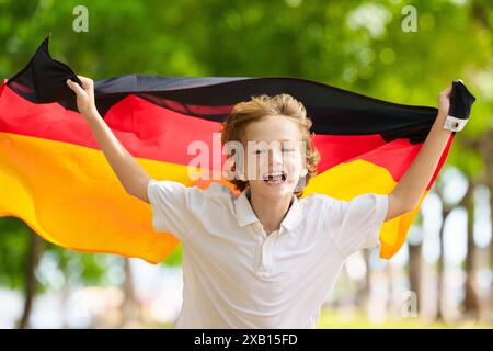 Kind läuft mit Deutschland-Flagge. Kleiner deutscher Junge, der die Country-Mannschaft anfeuert. Deutschland-Fans auf dem Sportplatz beobachten das Team. Familienfeiern Stockfoto