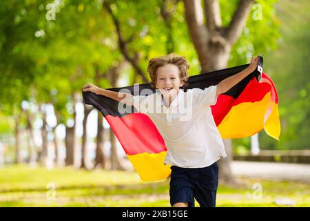 Kind läuft mit Deutschland-Flagge. Kleiner deutscher Junge, der die Country-Mannschaft anfeuert. Deutschland-Fans auf dem Sportplatz beobachten das Team. Familienfeiern Stockfoto