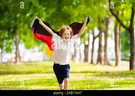 Kind läuft mit Deutschland-Flagge. Kleiner deutscher Junge, der die Country-Mannschaft anfeuert. Deutschland-Fans auf dem Sportplatz beobachten das Team. Familienfeiern Stockfoto