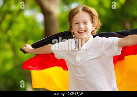 Kind läuft mit Deutschland-Flagge. Kleiner deutscher Junge, der die Country-Mannschaft anfeuert. Deutschland-Fans auf dem Sportplatz beobachten das Team. Familienfeiern Stockfoto