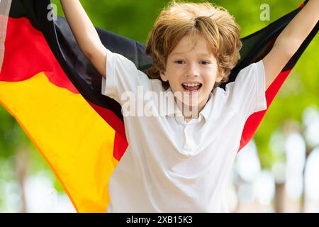 Kind läuft mit Deutschland-Flagge. Kleiner deutscher Junge, der die Country-Mannschaft anfeuert. Deutschland-Fans auf dem Sportplatz beobachten das Team. Familienfeiern Stockfoto