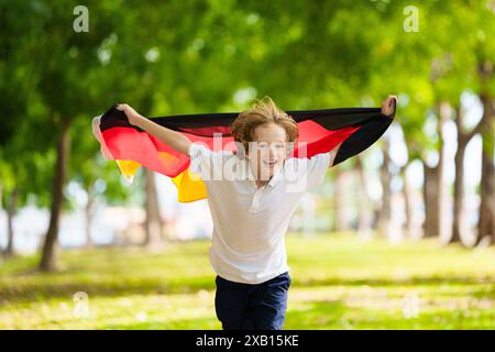 Kind läuft mit Deutschland-Flagge. Kleiner deutscher Junge, der die Country-Mannschaft anfeuert. Deutschland-Fans auf dem Sportplatz beobachten das Team. Familienfeiern Stockfoto