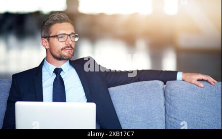 Business, Mann und Denken auf Sofa mit Laptop im Büro, nachdenklich und Vision für Online-Website oder nachdenklich auf Sofa. Professionell, Karriere und Stockfoto