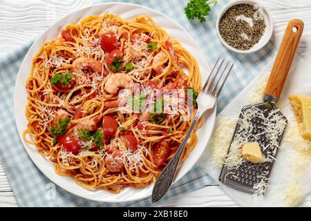 Garnelen fra diavolo mit Spaghetti, Tomatensoße, bestreut mit geriebenem Parmesankäse auf weißer Platte auf weißem Holztisch mit Gabel, Horizo Stockfoto