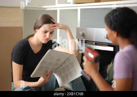 Zwei beunruhigte Mitbewohner, die Küchenmöbel zusammenbauen und das Installationshandbuch überprüfen Stockfoto