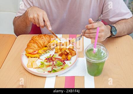 Mann isst Brioche Croissant Sandwich mit Minzlimonade Drink in einem Café. Stockfoto