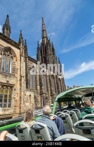 Eine Gruppe von Touristen, die in einem Bus mit offenem Oberdeck sitzen und an der Tolbooth Kirk auf der Royal Mile in Edinburgh vorbeifahren Stockfoto