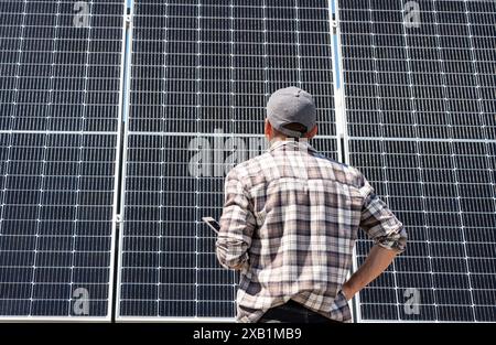 Rückansicht des Technikers der Solaranlage überprüft die Wartung der Solaranlagen. Der Mann steht vor Solarpaneelen und sieht sie an. Stockfoto
