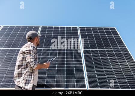 Die Tiefwinkelansicht des Technikers der Solaranlage überprüft die Wartung der Solarpaneele. Foreman mit digitalem Tablet vor einem großen Solarpanel. Stockfoto