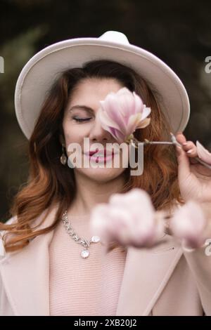 Die Frau hält Magnolienblüten, umgeben von blühenden Bäumen. Im Frühling mit natürlicher Schönheit und saisonalem Wandel Stockfoto