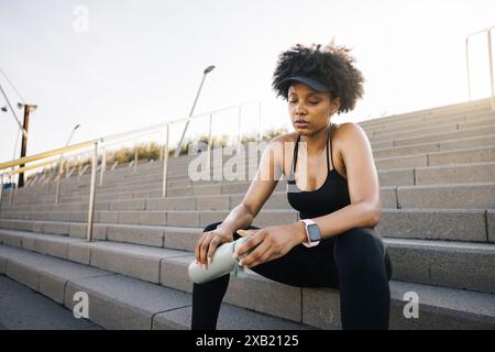 Junge müde Frau, die nach einem Workout eine Pause macht und sich auf den Stufen ausruht, nachdenklich und nachdenklich wirkt. Stockfoto