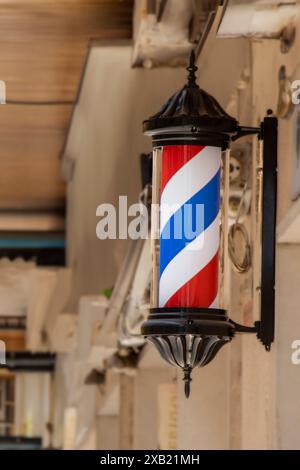 Ein klassisches Friseurpfosten-Schild mit roten, weißen und blauen Streifen vor einem Friseurladen in einem Stadtgebiet. Stockfoto