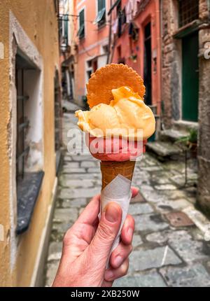 Hand hält Eis in der farbenfrohen engen Straße in Cinque Terre, Italien. Stockfoto